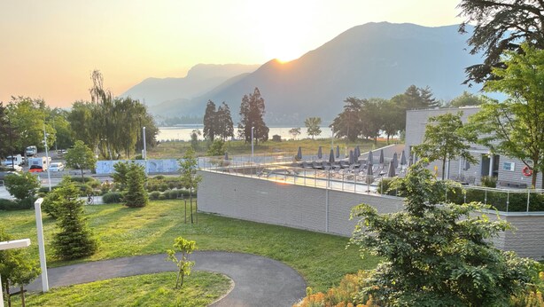 A landscaped area with a curved pathway, a pool with lounge chairs, and a view of a lake and mountains in the background. - L'Estrade 4* - Appartement 2 bedrooms with the view lake & garage (Annecy)