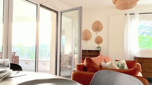 A dining area with a table set for two, a sliding glass door leading to a balcony, and a red sofa in the background. - L'Estrade 4* - Appartement 2 bedrooms with the view lake & garage (Annecy)