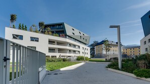 A modern building with a flat roof, multiple balconies, and a paved entrance area with greenery. - L'Estrade 4* - Appartement 2 bedrooms with the view lake & garage (Annecy)