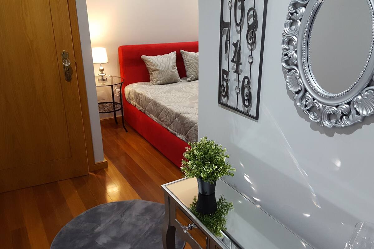 A bedroom with a red sofa, a mirror, and a small potted plant.
