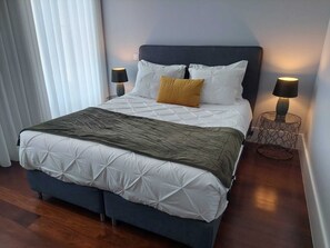 A neatly made bed with a dark headboard, white bedding, and a mustard-colored pillow. There are two bedside lamps on metal stands. - Cool Guesthouse (Porto)