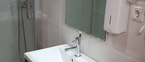 A bathroom with a glass shower enclosure, a white sink with a modern faucet, a dark cabinet below the sink, and a mirror above the sink.