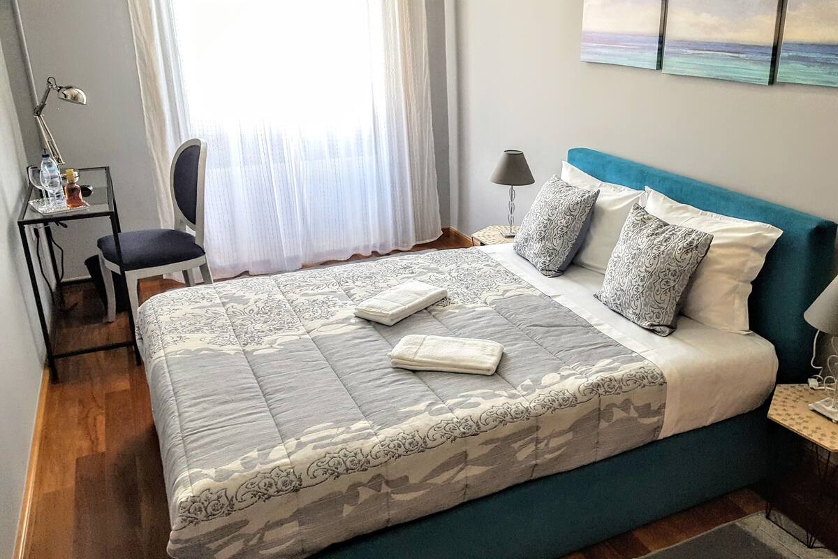A neatly arranged bedroom with a bed, two bedside tables, a chair, and a desk.
