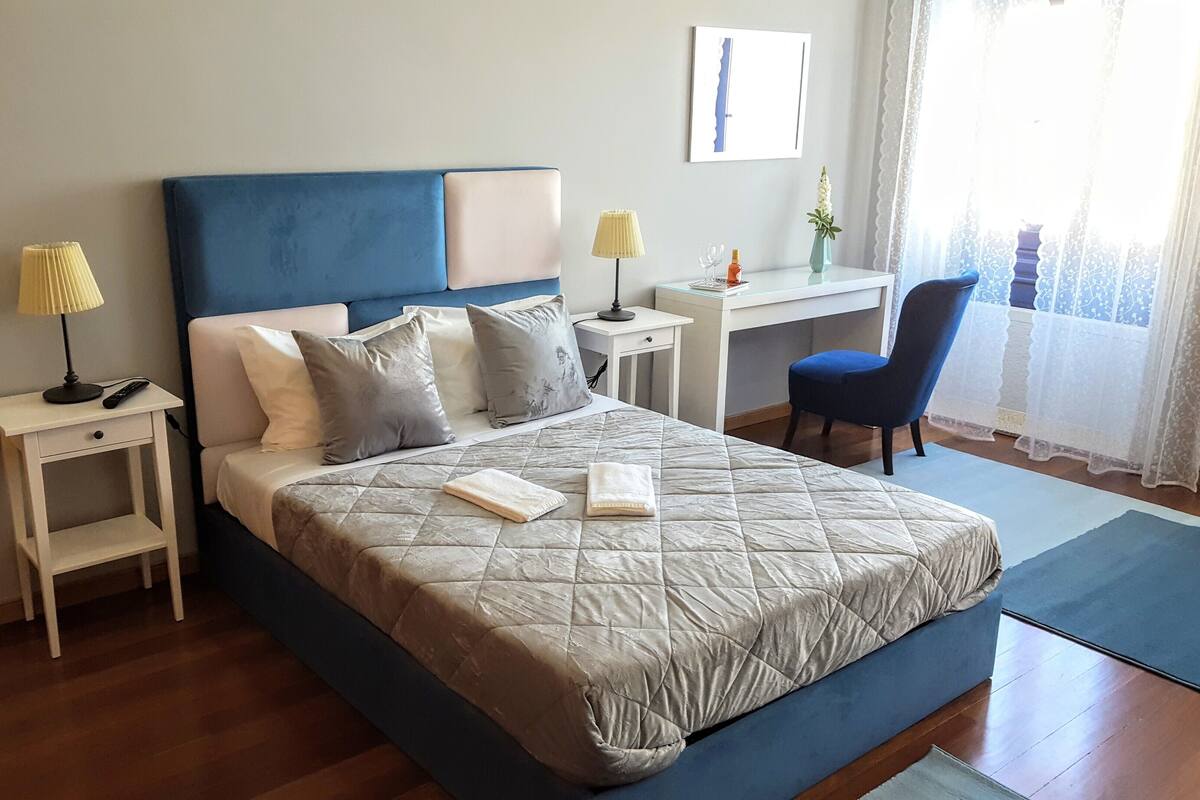 A neatly arranged bedroom with a bed, bedside tables, a desk, and a chair.