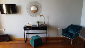 A modern living room with a black desk, a teal ottoman, a blue chair, a round mirror, and a flat-screen TV on the wall. - Cool Guesthouse (Porto)