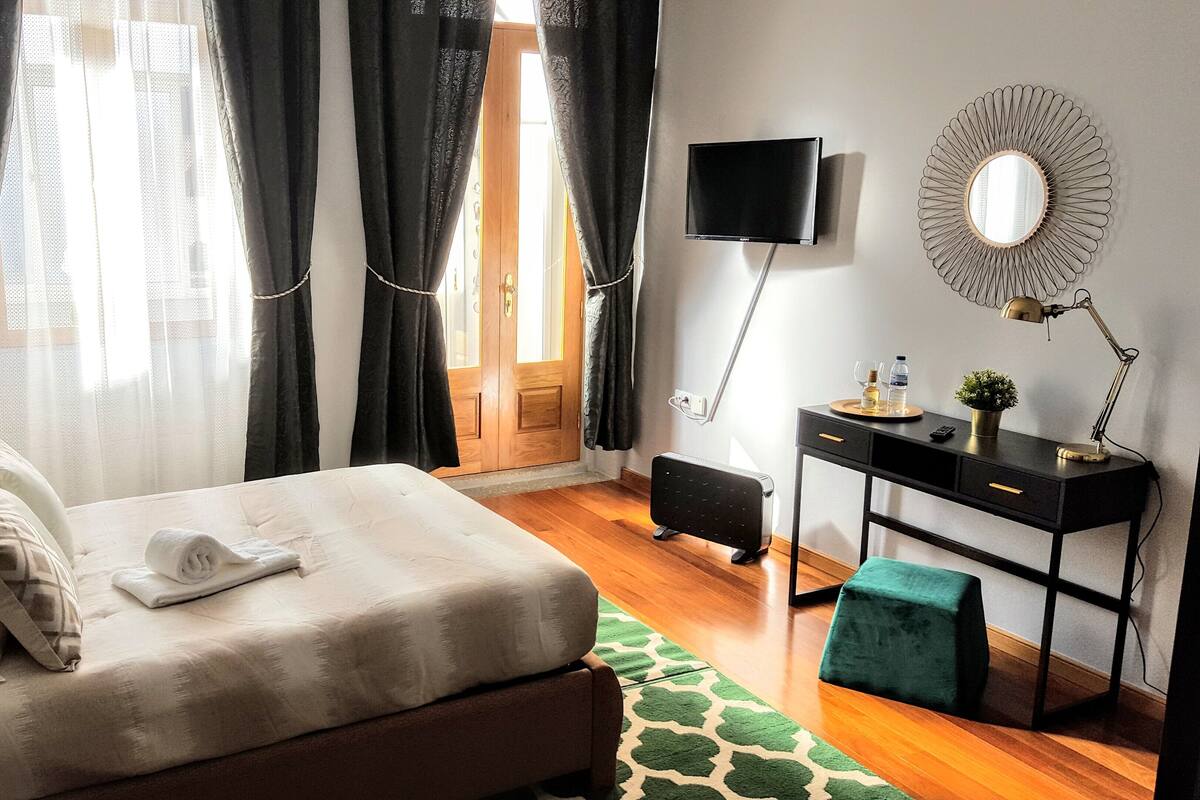A neatly arranged bedroom with a bed, a desk, a TV, and a mirror.
