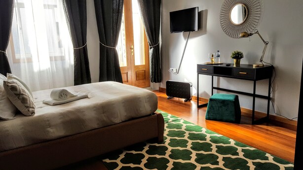 A neatly arranged bedroom with a bed, a desk, a chair, a TV, and a mirror. - Cool Guesthouse (Porto)