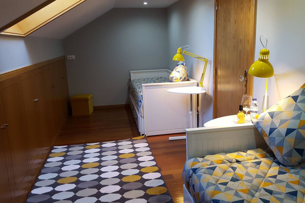 A compact bedroom with a bed, bedside table, lamp, and a small white dresser.
