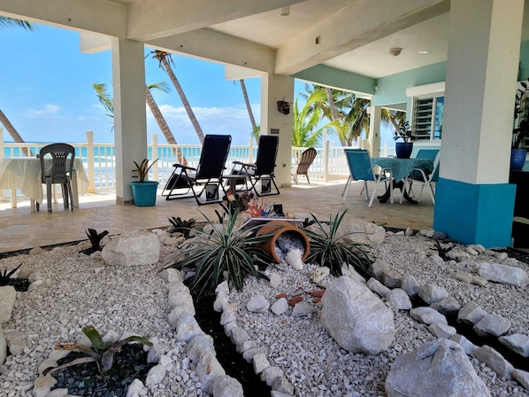 A covered outdoor area with lounge chairs, a small water feature, and a view of the ocean.