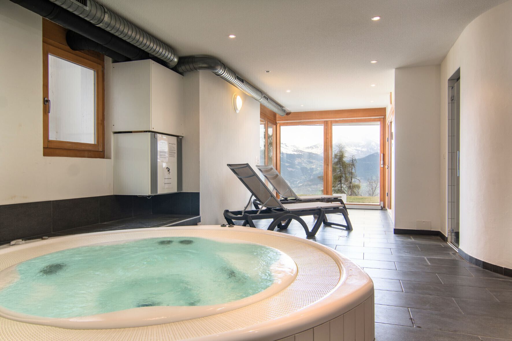 Ein Wellnessbereich mit Whirlpool, Sauna und Liegestuhl mit Blick auf die Berge.