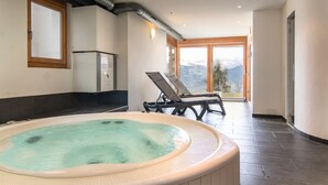 Un espace bien-être comprenant un bain à remous, un sauna et un fauteuil relaxant avec vue sur la montagne.