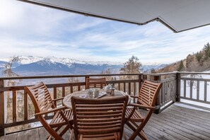 Un terrazza in legno con un tavolo rotondo e sedie, con vista su una catena montuosa innevata.