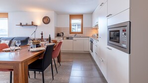Une cuisine moderne avec des armoires blanches, un four encastré et un coin repas comprenant une table et des chaises en bois.