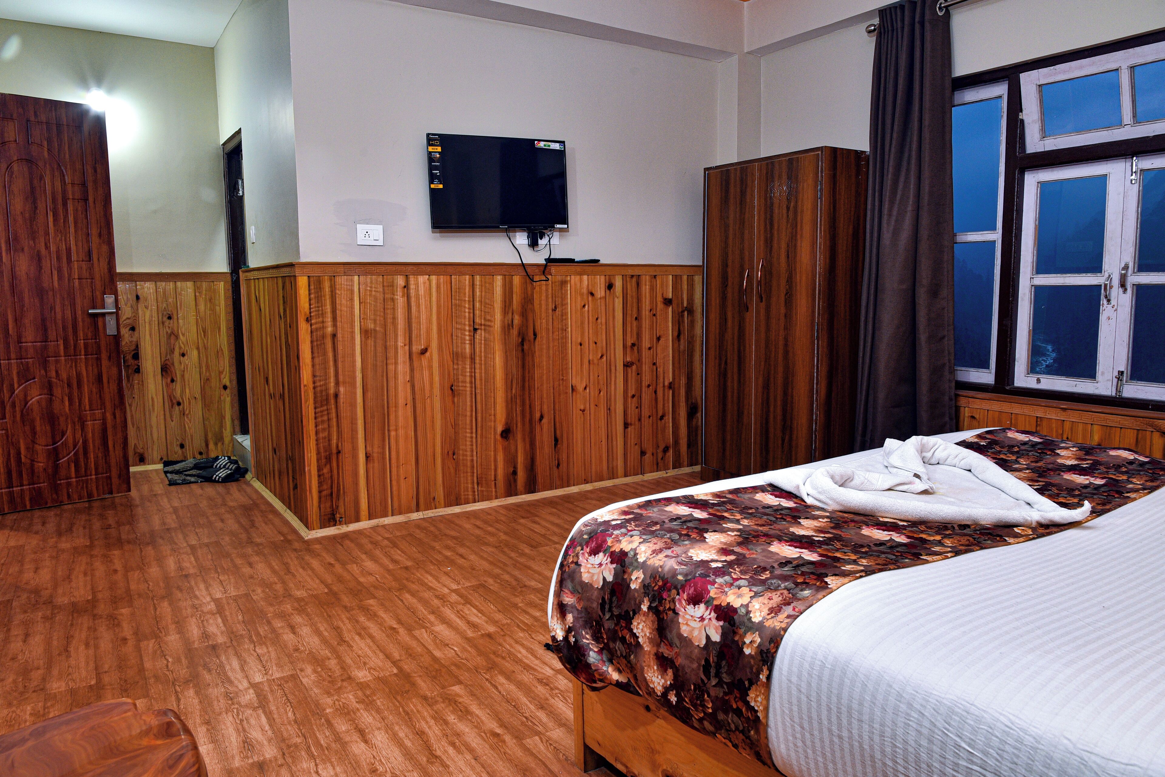 A hotel room with a wooden wardrobe, a bed with a floral bedspread, and a television mounted on the wall.