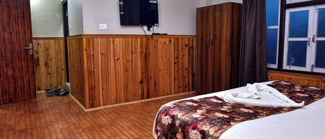 A hotel room with a wooden wardrobe, a bed with a floral bedspread, and a television mounted on the wall.