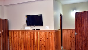 A room with a wooden panel wall, a mounted flat-screen TV, and a wooden door. - Rufina Lachen Deezong (Chungthang)