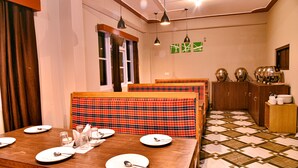 A dining area with a wooden table set for four, a plaid table runner, and a patterned floor. - Rufina Lachen Deezong (Chungthang)