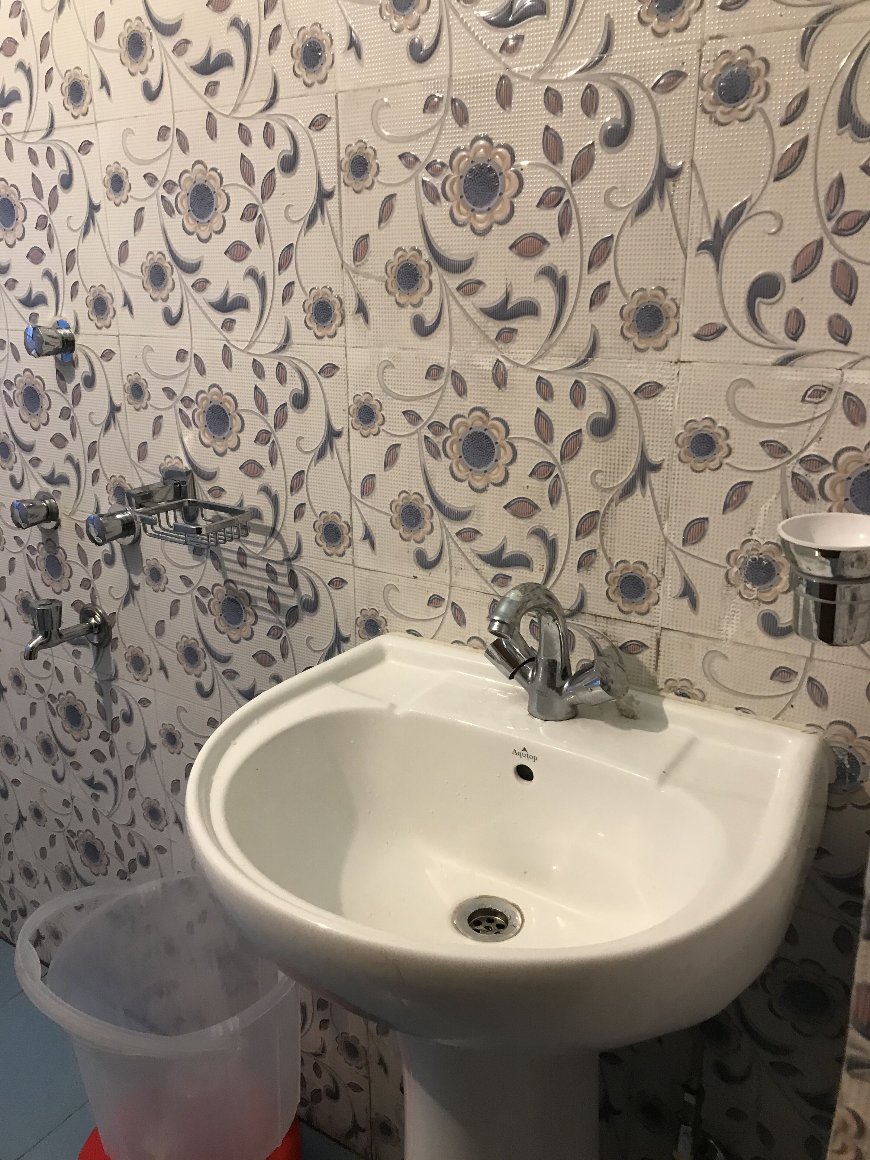 A bathroom with a white sink, a mirror, and a trash bin. The walls have a floral tile pattern.