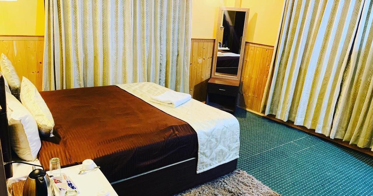 Une chambre d’hôtel avec un lit, une table de chevet, un miroir et des rideaux.