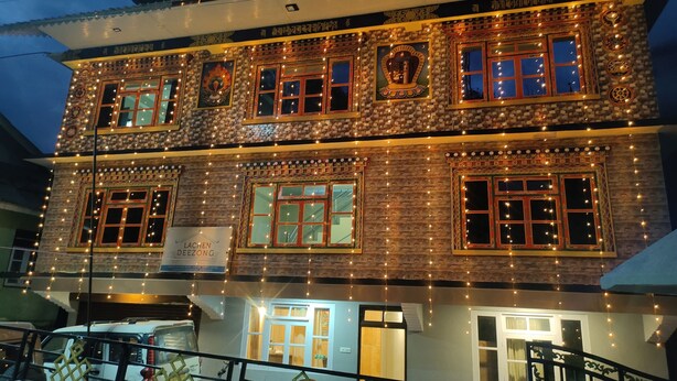 A two-story building with multiple windows, some adorned with string lights. - Rufina Lachen Deezong (Chungthang)