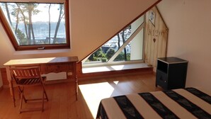 Een kamer met een schuine plafond, een bureau met stoel, een bed en een klein kastje.