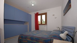 Una camera da letto con un letto, una scrivania, una sedia, una finestra con tende e una lampada a muro.