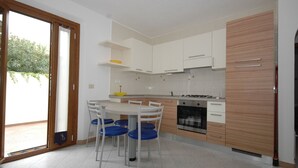 Una cucina moderna con mobili bianchi, un'isola centrale con sedie blu e una porta scorrevole in vetro che dà su un patio.