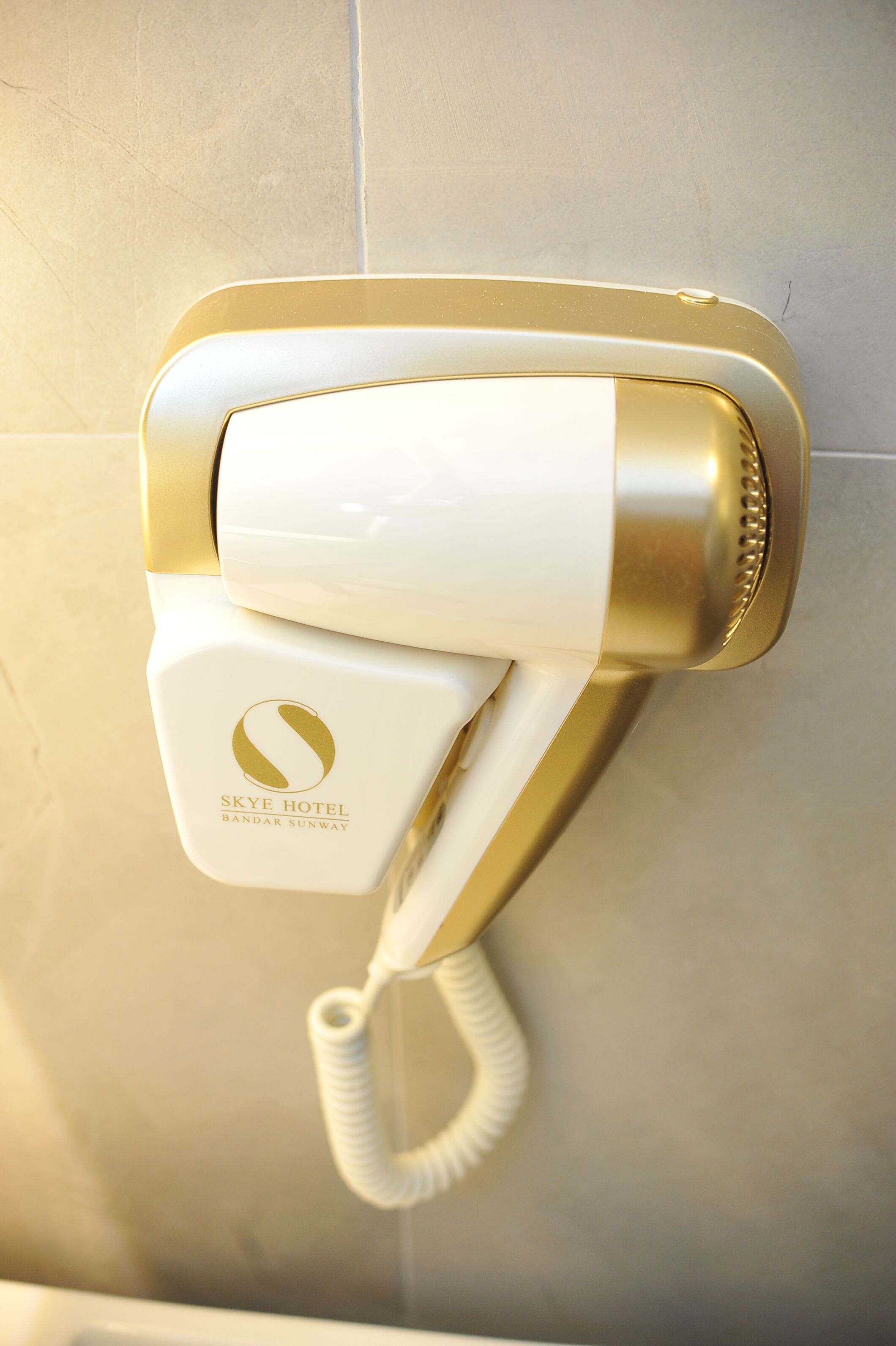 A wall-mounted hair dryer with a gold and white design, featuring the Skye Hotel logo.