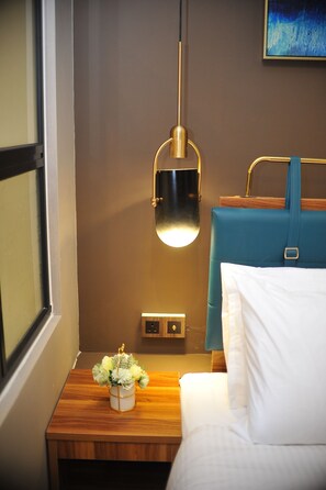 Een hotelkamer met een bed, een nachtkastje met een lamp, een aan de muur hangend schilderij en een raam.