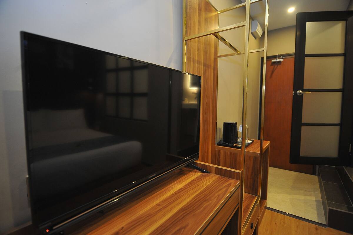 Une chambre moderne dotée d’un grand téléviseur à écran plat posé sur un meuble en bois, d’une armoire en bois et d’une porte coulissante donnant accès à une salle de bain.