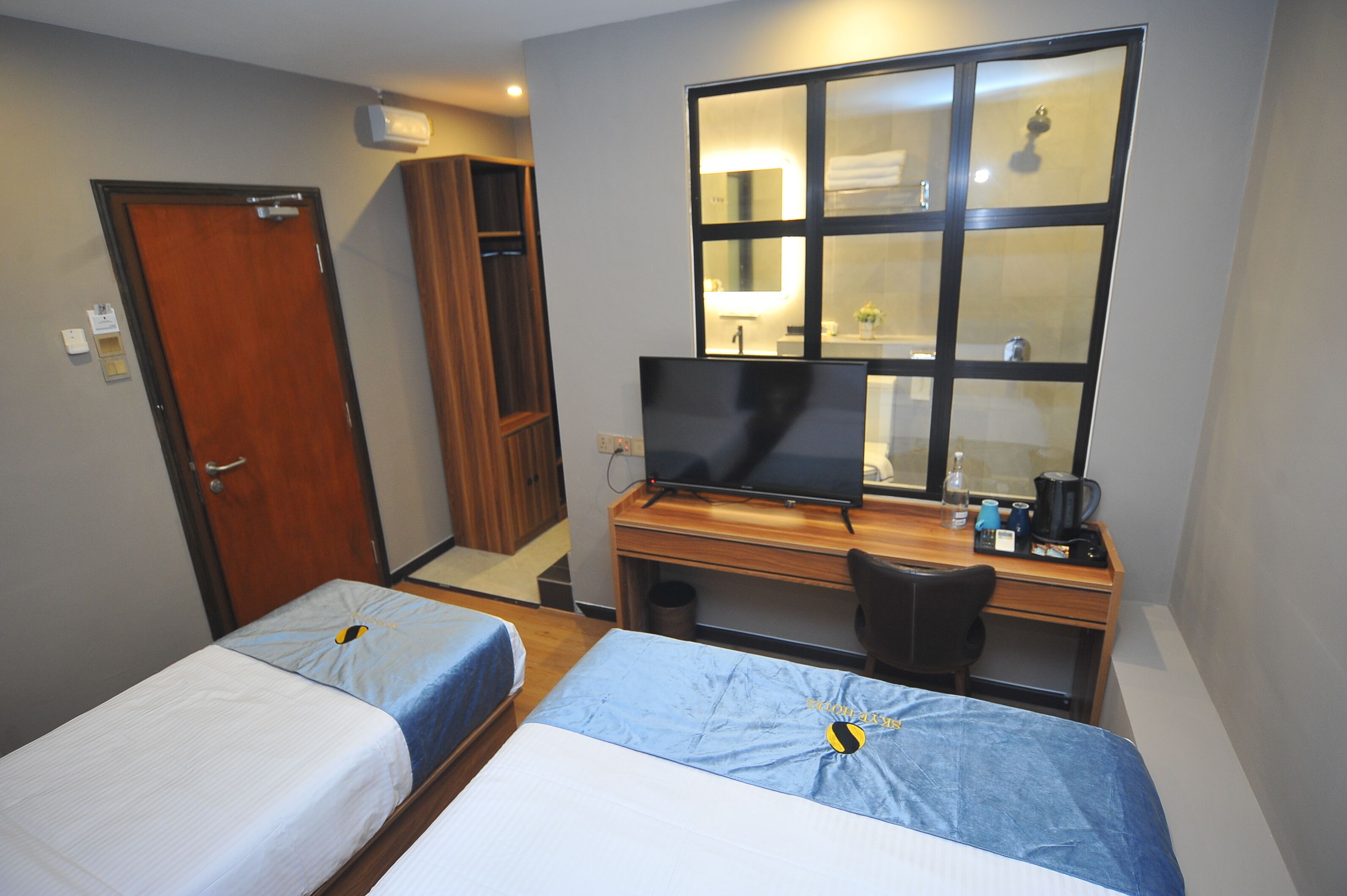 Habitación de hotel con dos camas, un escritorio con ordenador, televisor y un espejo grande.