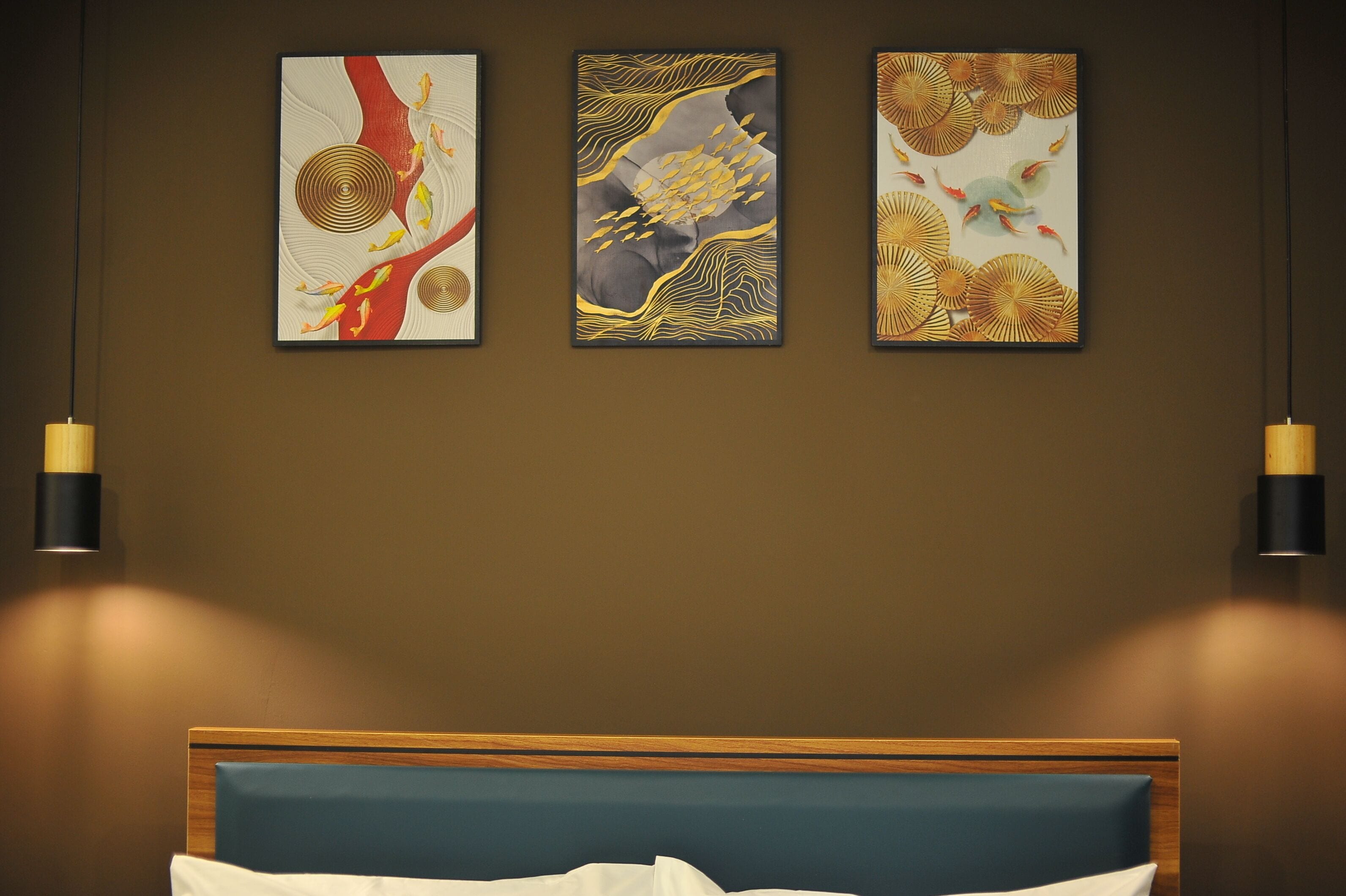 A hotel room with a bed, three wall-mounted paintings, and two pendant lights.
