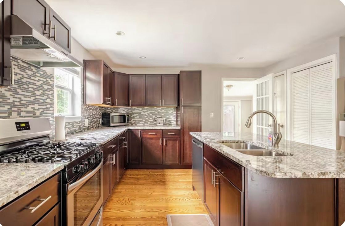 A modern kitchen with dark wood cabinets, a granite countertop, and a stainless steel range hood.