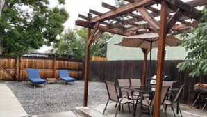 Un patio cubierto con mesa y sillas, una pérgola y una silla de descanso azul.