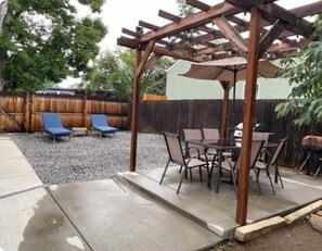 Un patio cubierto con mesa y sillas, una pérgola y una silla de descanso azul.
