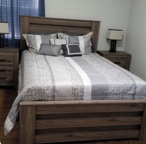 Quarto com cama de madeira, mesa de cabeceira, luminária e janela com cortinas.