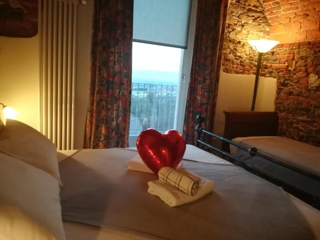 Una camera d'albergo con un letto, una decorazione a forma di cuore, un asciugamano arrotolato, una finestra con vista e una lampada.