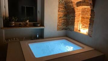 A bathroom with a large bathtub, a window, and a brick wall.
