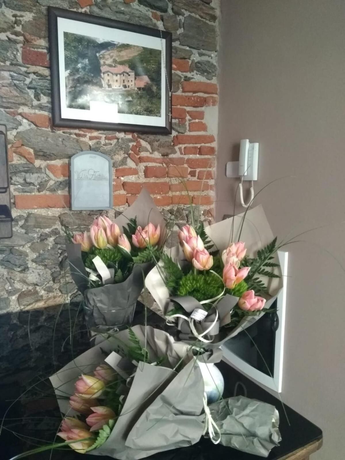 Um arranjo de flores rosa e amarelo sobre uma mesa, em frente a uma parede de pedra com um quadro e uma placa.