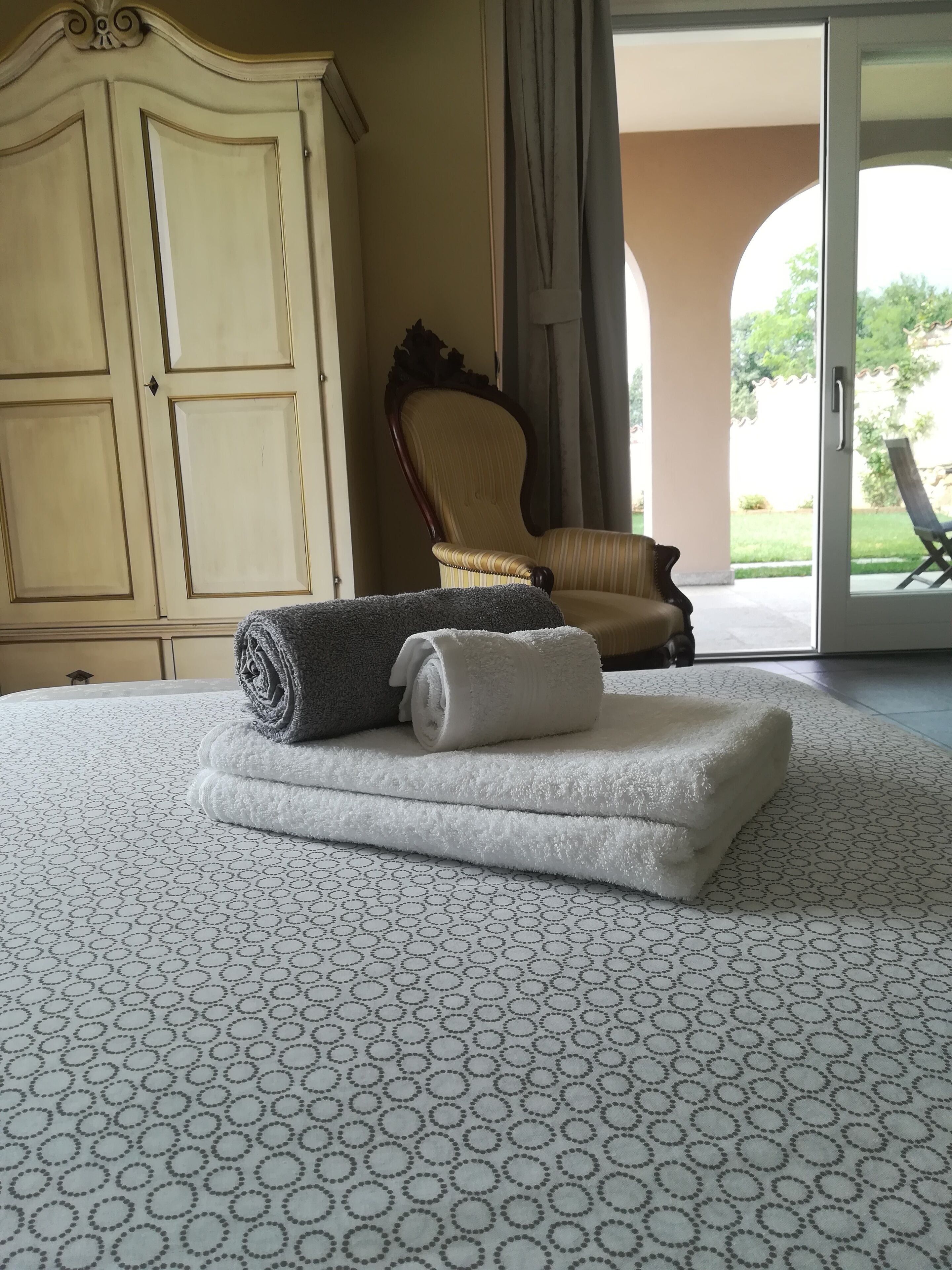 Una cama bien hecha con toallas enrolladas, un armario espacioso y una silla junto a un ventanal corredero que da a un área exterior.