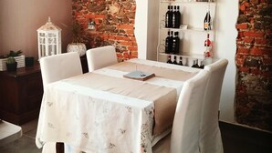 A dining area with a table set for two, a white clock on the wall, and a wine rack with bottles. - B&B Villa Antilia (Busca)