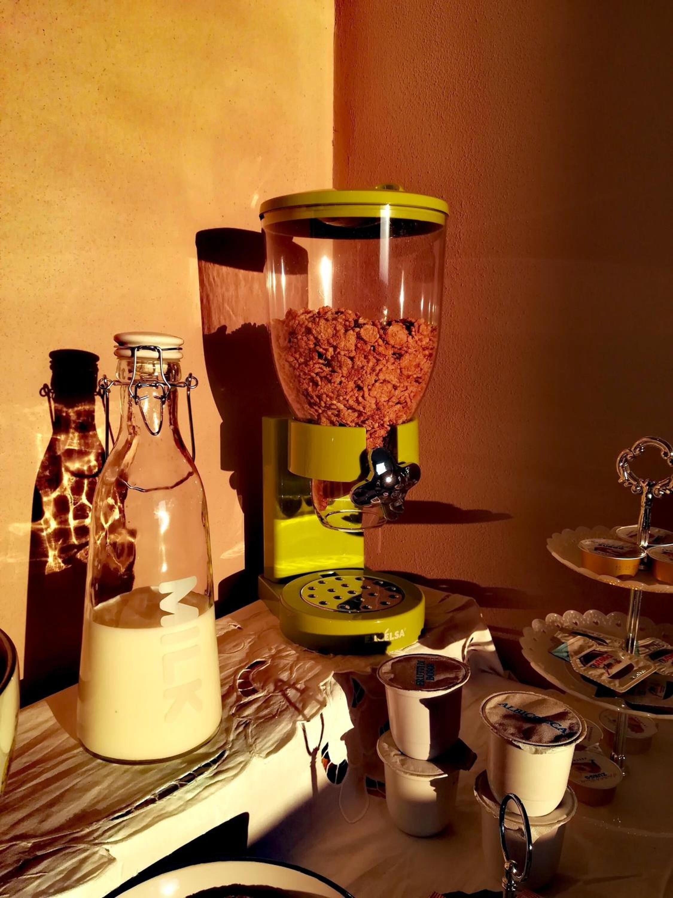 Buffet d'esmorzars preparat amb un dispensador de cereals, ampolles de llet i diferents aliments sobre una taula.