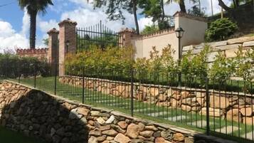 Un'area giardino recintata con un muro in pietra, una palma e un edificio con tetto in tegole.