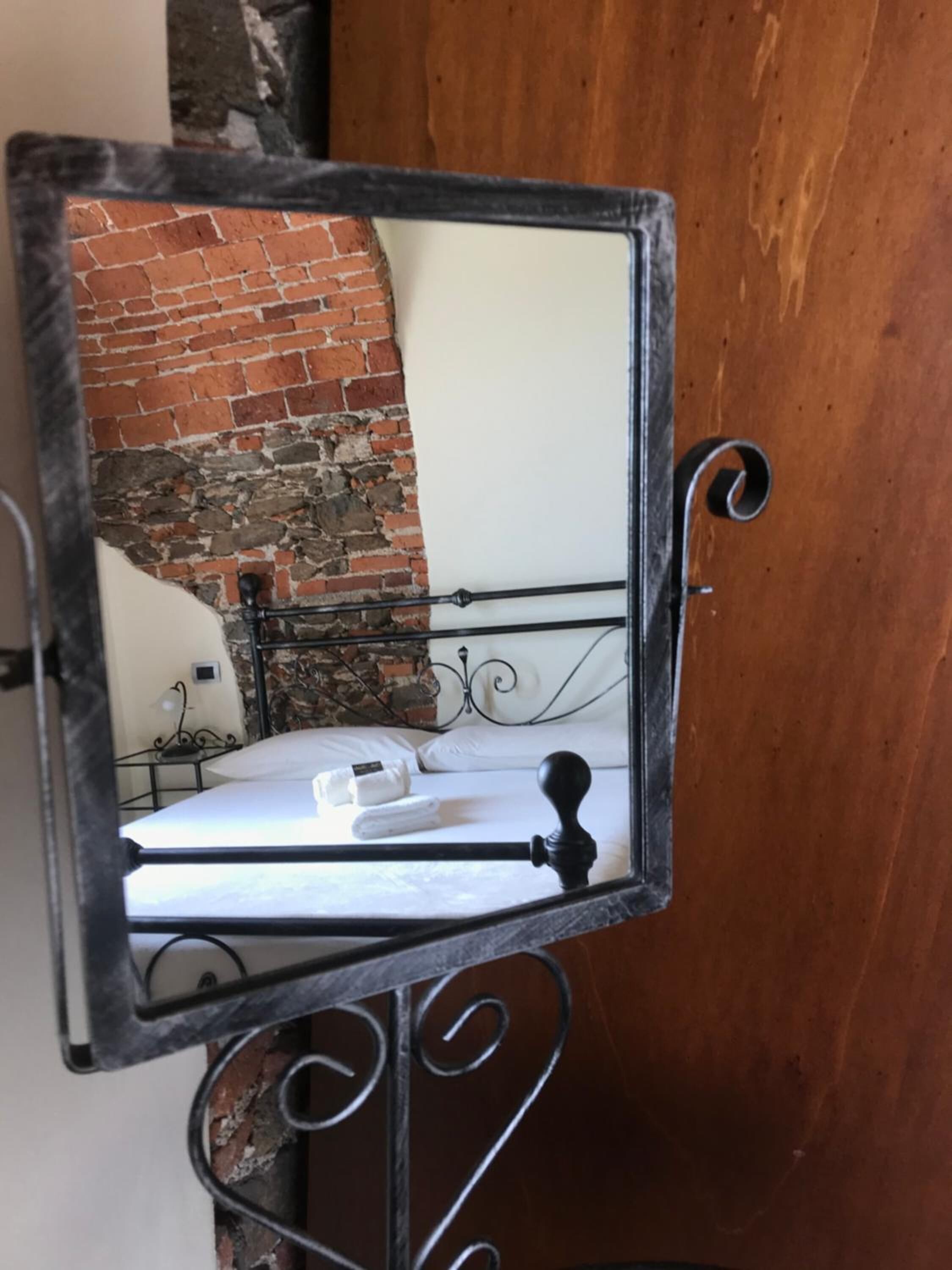 A mirror with a black frame reflecting a bed with white bedding and a brick wall.