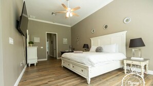A bedroom with a large bed, a ceiling fan, a TV, and a nightstand with a lamp. - Oviedo Charmer - Heated Pool - Close to everything (Oviedo)