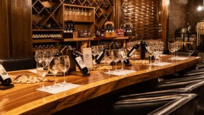 Una zona de bar con mostrador de madera, botellas de vino, copas y una estantería para vinos al fondo.