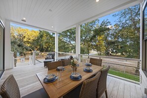 A covered outdoor dining area with a wooden table set for six, surrounded by wicker chairs.