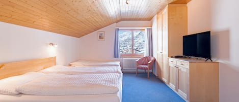 Quarto com três camas de madeira, televisão e janela com vista para montanhas cobertas de neve.