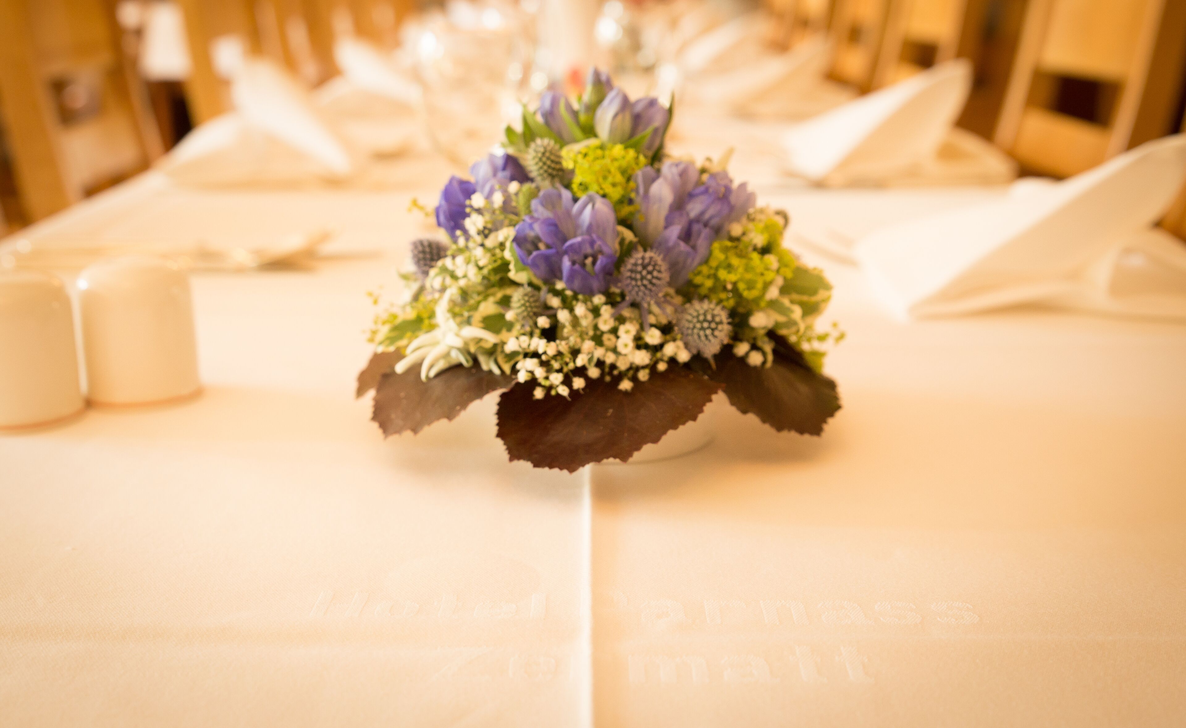 Una mesa con un centro de flores, servilletas blancas y velas.