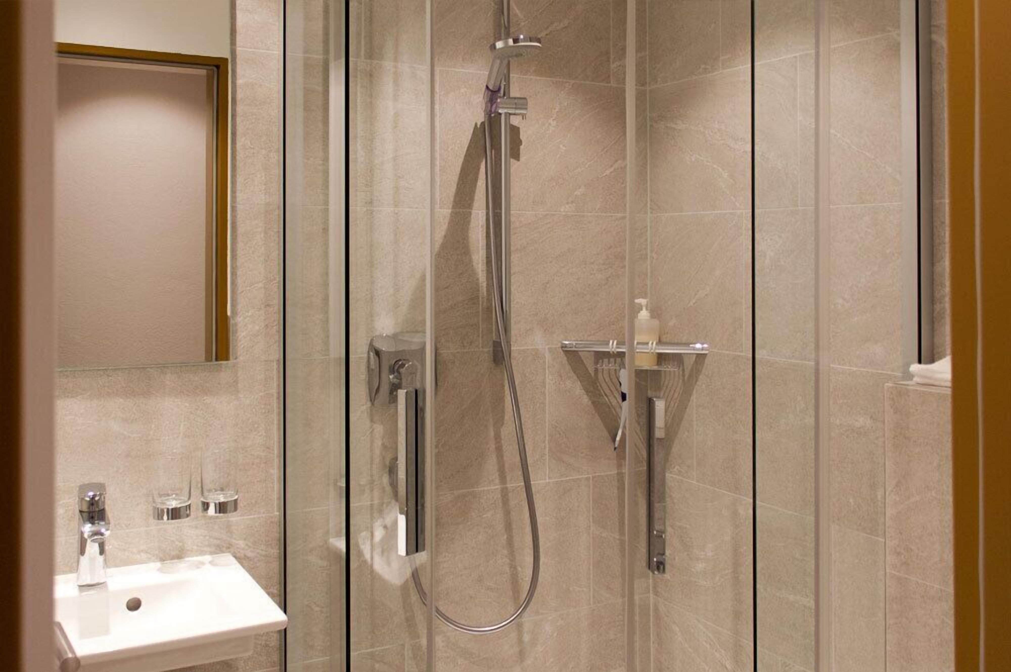 Een badkamer met een douche met glazen wand, een wastafel met spiegel en een zeepdispenser.